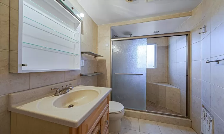 Bathroom with toilet, tile walls, tile patterned floors, and a shower with door