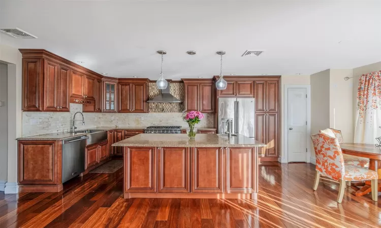 Kitchen featuring a center island, decorative light fixtures, wall chimney range hood, stainless steel appliances, and sink