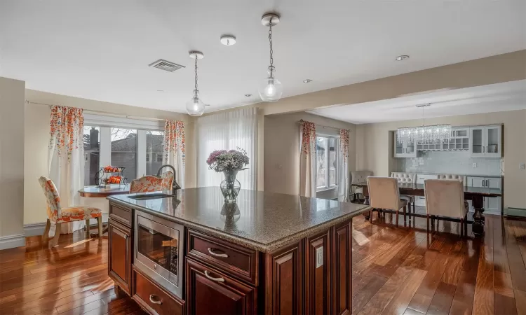 Kitchen featuring a center island with sink, stainless steel microwave, dark hardwood / wood-style flooring, pendant lighting, and sink