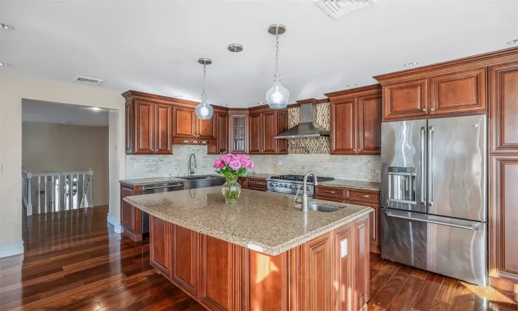 Kitchen featuring wall chimney exhaust hood, decorative light fixtures, stainless steel appliances, sink, and light stone counters