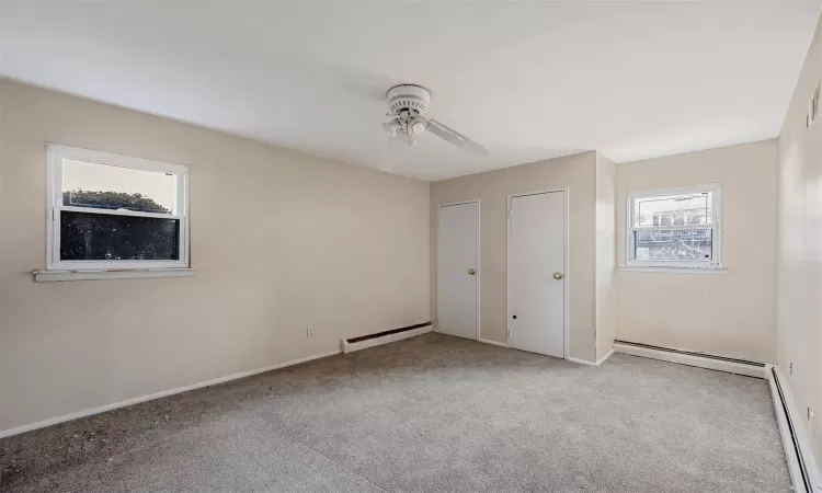 Unfurnished bedroom featuring ceiling fan, a baseboard radiator, light colored carpet, and two closets