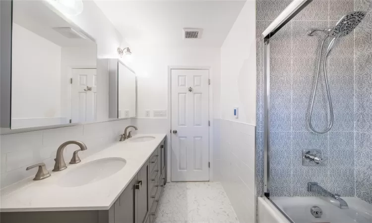 Bathroom with tile patterned floors, tile walls, tasteful backsplash, shower / bath combination with glass door, and vanity