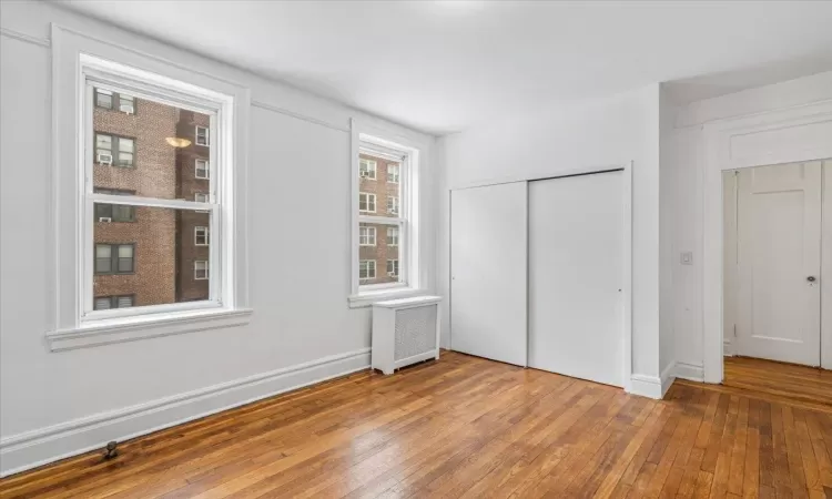 Unfurnished bedroom featuring radiator, hardwood  floors, and a large closet