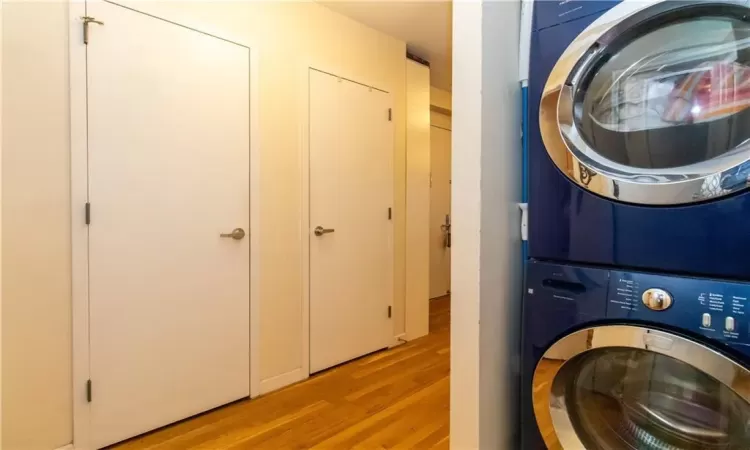 Laundry room with light hardwood / wood-style flooring and stacked washing maching and dryer