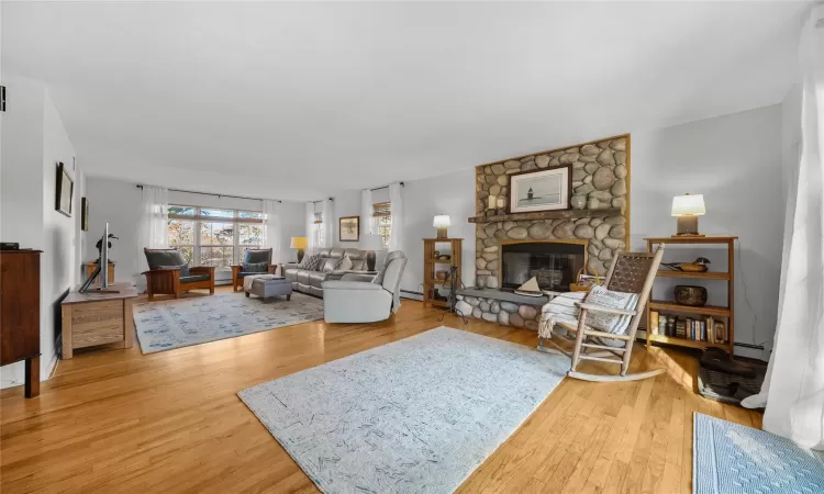 Living room with hardwood / wood-style flooring, a stone fireplace, and a baseboard radiator