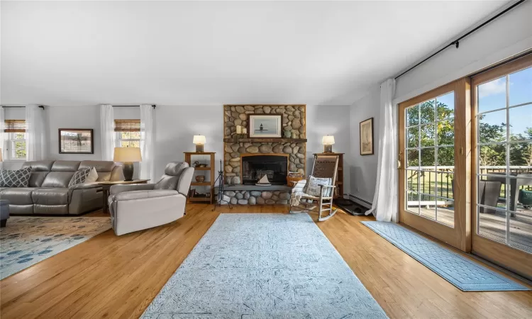 Living room with a stone fireplace, light wood-type flooring, and baseboard heating