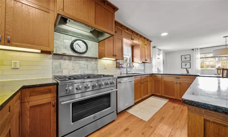 Kitchen featuring sink, tasteful backsplash, kitchen peninsula, appliances with stainless steel finishes, and light wood-type flooring