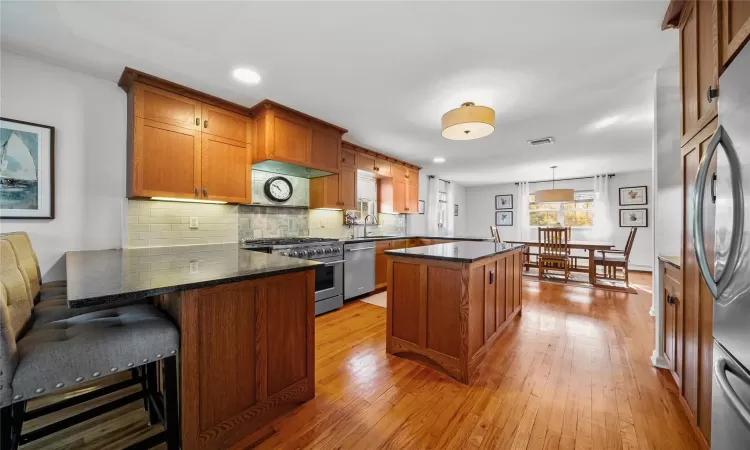 Kitchen featuring a kitchen breakfast bar, stainless steel appliances, decorative light fixtures, light hardwood / wood-style flooring, and a center island