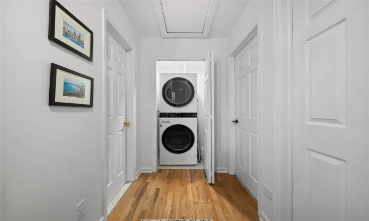 Clothes washing area with stacked washing maching and dryer and light hardwood / wood-style floors