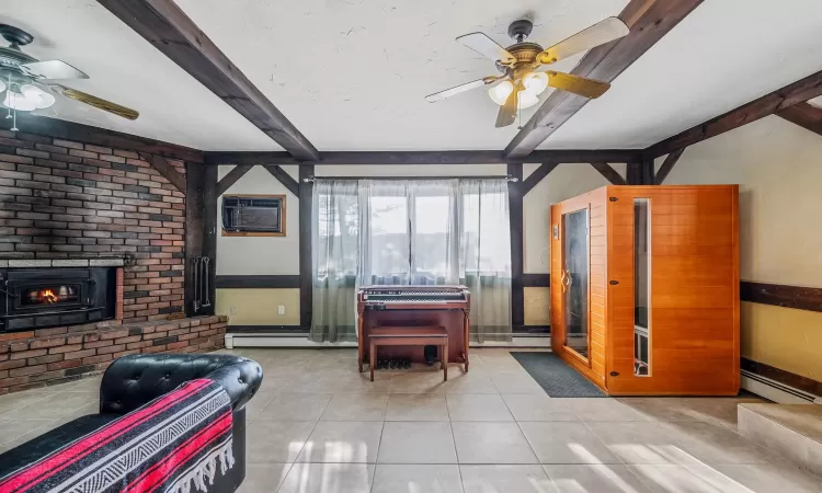 Tiled living room featuring beamed ceiling, ceiling fan, a fireplace, and a wall unit AC