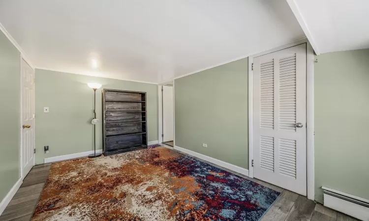 Unfurnished bedroom featuring a baseboard heating unit and dark hardwood / wood-style floors