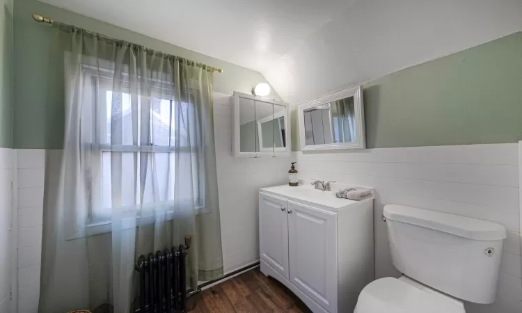 Bathroom featuring radiator, wood-type flooring, lofted ceiling, vanity, and toilet