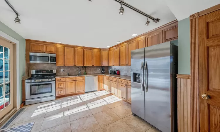 Kitchen featuring light tile patterned floors, decorative backsplash, sink, and appliances with stainless steel finishes