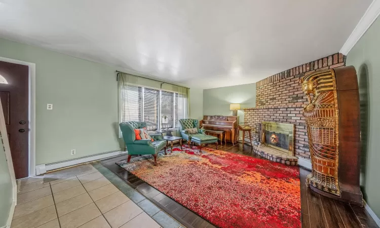 Living room featuring baseboard heating, tile patterned flooring, and a brick fireplace