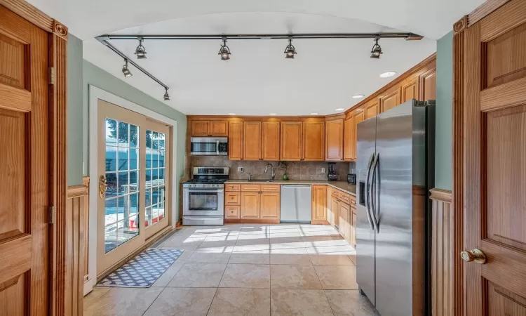 Kitchen with light tile patterned floors, decorative backsplash, sink, and appliances with stainless steel finishes