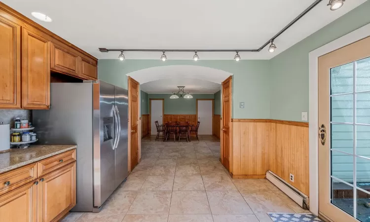 Kitchen featuring wood walls, a baseboard radiator, light tile patterned floors, light stone counters, and stainless steel fridge with ice dispenser