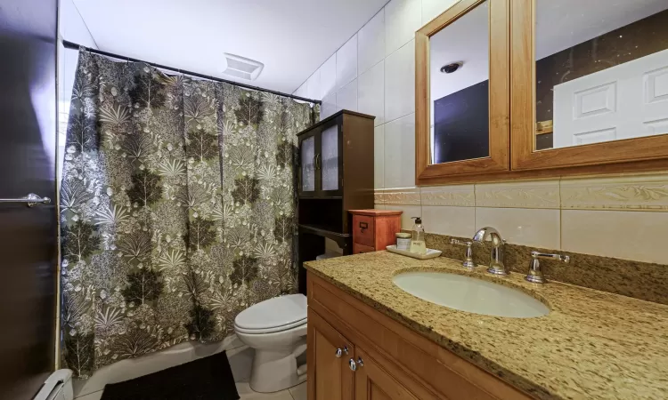 Bathroom featuring tasteful backsplash, tile walls, vanity, a baseboard heating unit, and toilet