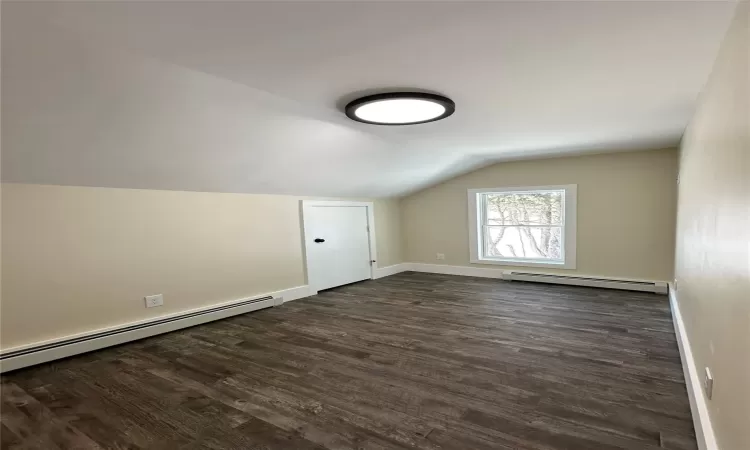 Additional living space featuring lofted ceiling, dark wood-type flooring, and a baseboard radiator