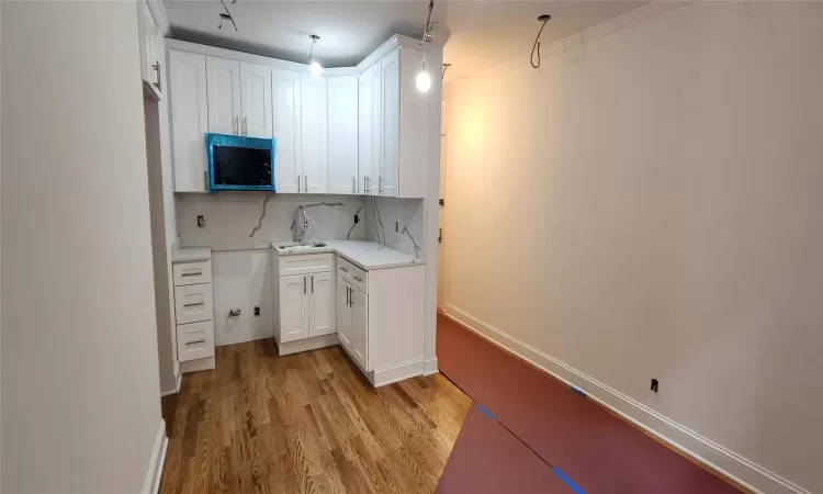 Kitchen featuring tasteful backsplash, white cabinetry, sink, light hardwood / wood-style floors, and crown molding