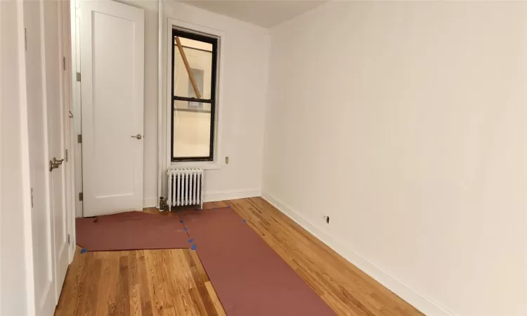 Unfurnished room featuring crown molding, radiator heating unit, and wood-type flooring