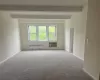 Carpeted empty room with beamed ceiling, radiator, and an AC wall unit