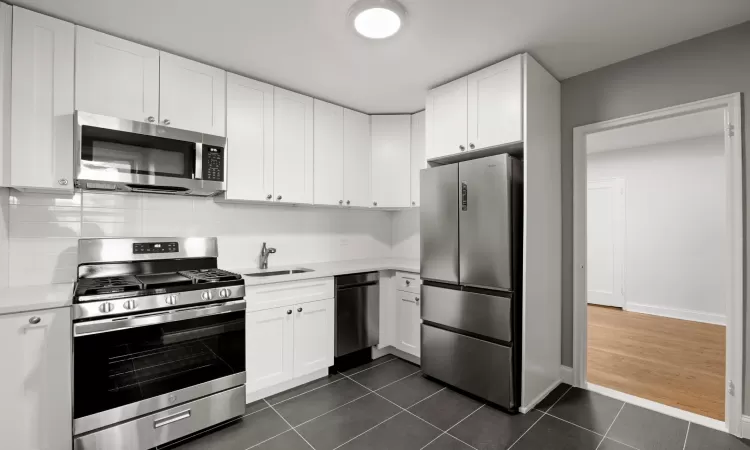 Kitchen featuring appliances with stainless steel finishes, dark tile patterned floors, and white cabinets