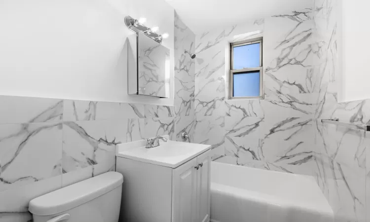 Full bathroom with vanity, toilet,  shower combination, and tile walls