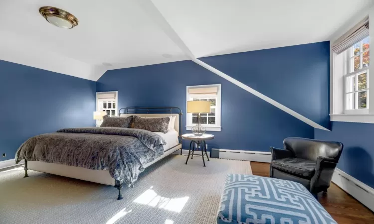 Bedroom with vaulted ceiling, a baseboard heating unit, and hardwood / wood-style floors