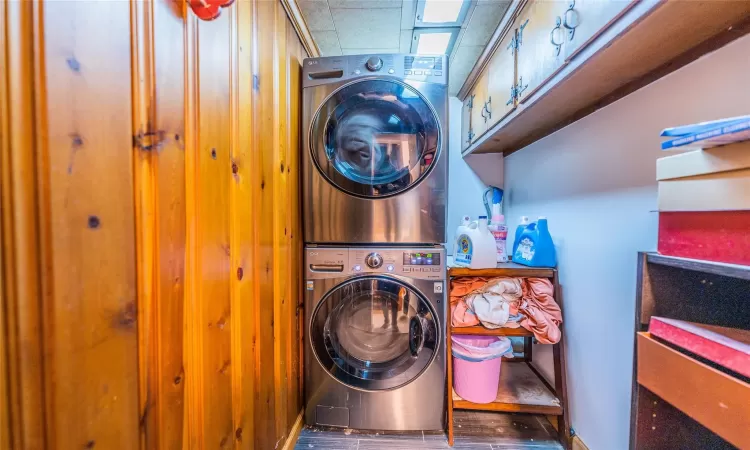 Laundry area featuring stacked washer / dryer, dark hardwood / wood-style floors, and cabinets