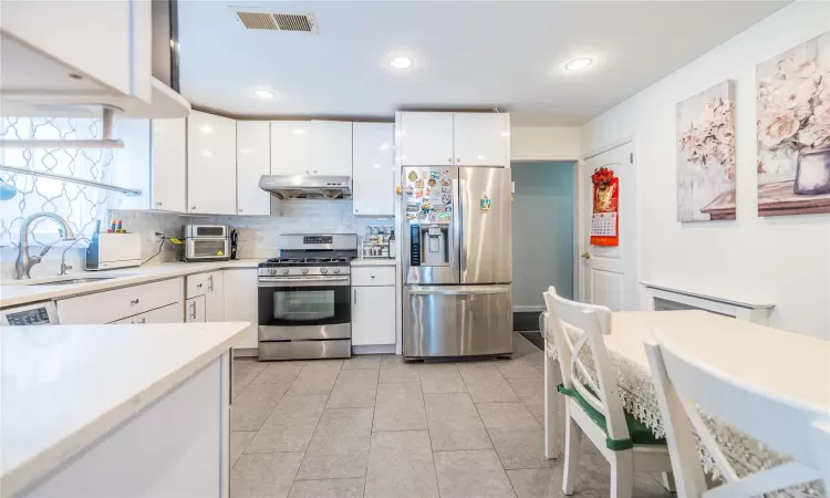 Kitchen featuring sink, light tile patterned floors, appliances with stainless steel finishes, white cabinetry, and tasteful backsplash