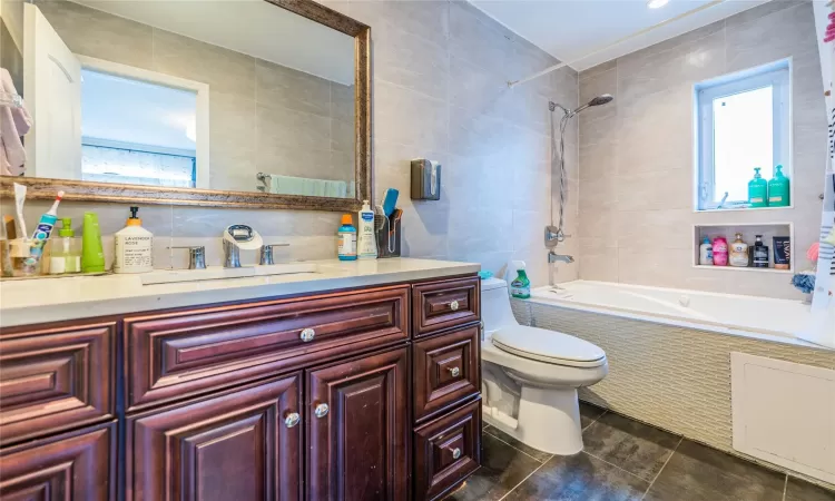 Full bathroom featuring tiled shower / bath, tile walls, vanity, and toilet