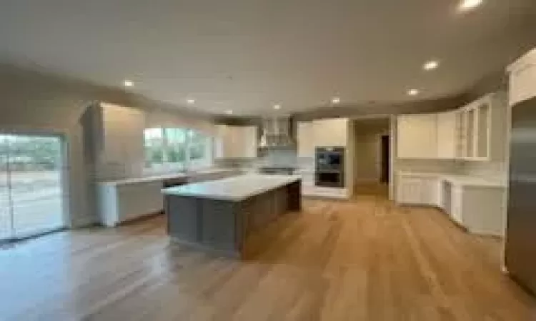 Kitchen featuring white cabinetry, double oven, a kitchen island, wall chimney exhaust hood, and light wood-type flooring