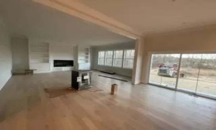 Unfurnished living room featuring ornamental molding, light wood-type flooring, and built in shelves