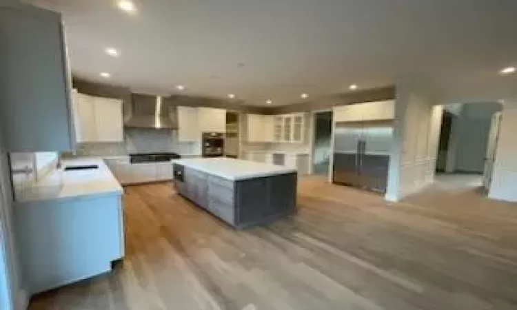 Kitchen with white cabinetry, high quality fridge, a kitchen island, oven, and wall chimney exhaust hood