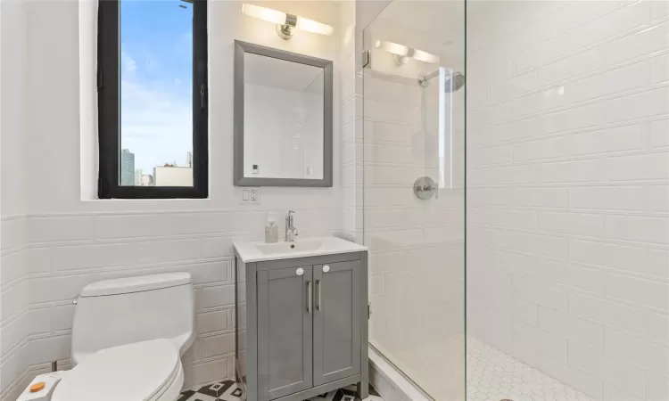 Bathroom with tiled shower, vanity, toilet, and tile walls