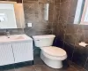 Bathroom with vanity, toilet, tile walls, and a wealth of natural light