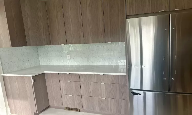 Kitchen with stainless steel refrigerator, decorative backsplash, and light stone counters