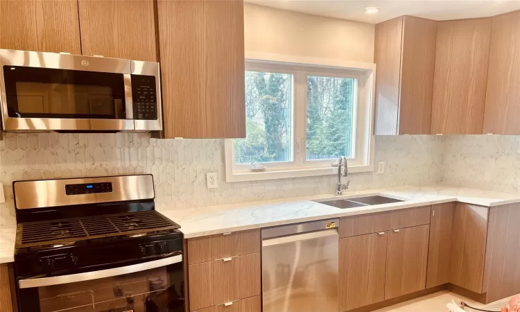 Kitchen featuring light stone counters, stainless steel appliances, sink, and backsplash