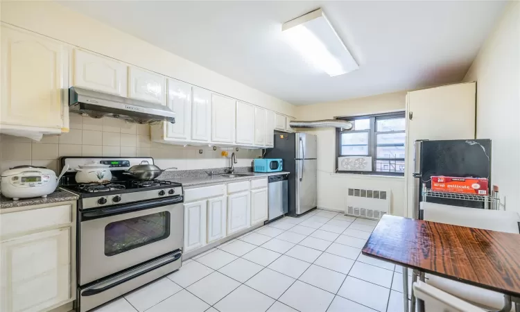 Kitchen with appliances with stainless steel finishes, backsplash, sink, exhaust hood, and radiator heating unit