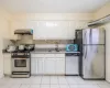 Kitchen with sink, backsplash, extractor fan, light tile patterned floors, and appliances with stainless steel finishes