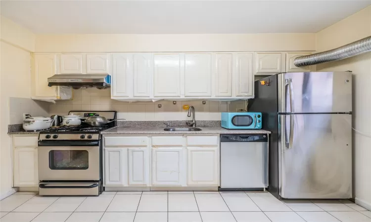 Kitchen with sink, backsplash, extractor fan, light tile patterned floors, and appliances with stainless steel finishes