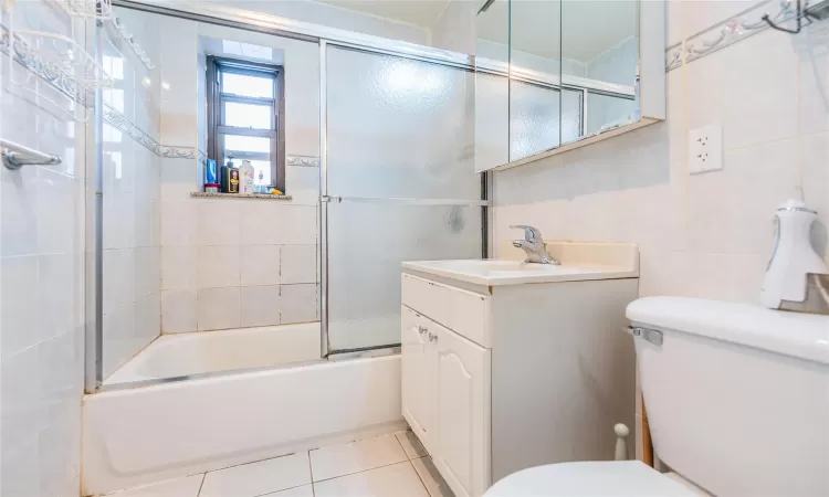 Full bathroom with combined bath / shower with glass door, tile patterned floors, vanity, tile walls, and toilet