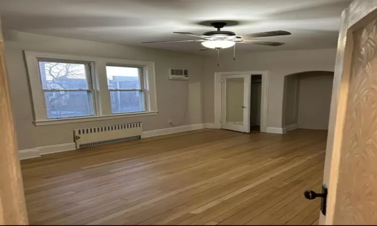 Spare room with ceiling fan, wood-type flooring, radiator, and a wall unit AC