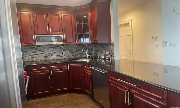 Kitchen with sink, backsplash, stainless steel appliances, and dark stone counters