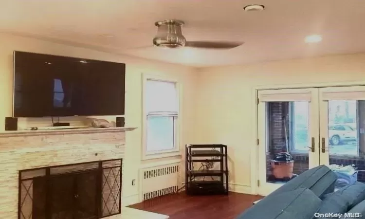 Living room featuring french doors, dark wood-type flooring, a stone fireplace, radiator, and ceiling fan