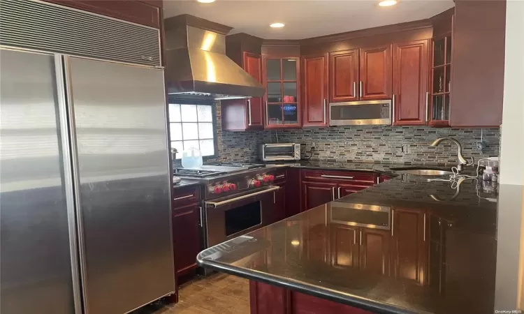 Kitchen featuring sink, extractor fan, appliances with stainless steel finishes, dark stone counters, and backsplash