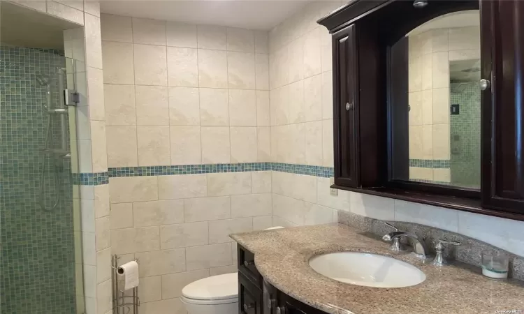 Bathroom featuring vanity, toilet, tile walls, and walk in shower