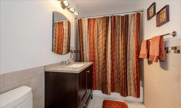 Full bathroom with toilet, tile walls, vanity, shower / bath combo, and tile patterned flooring