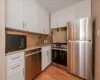 Kitchen with appliances with stainless steel finishes, sink, white cabinets, light stone countertops, and light wood-type flooring