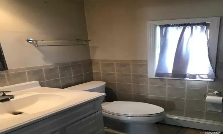 Bathroom with vanity, plenty of natural light, a baseboard heating unit, and tile walls